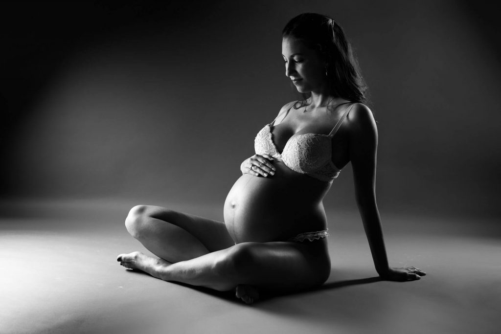 schwangere Frau sitzt auf dem Boden, Babybauchfoto in Wäsche