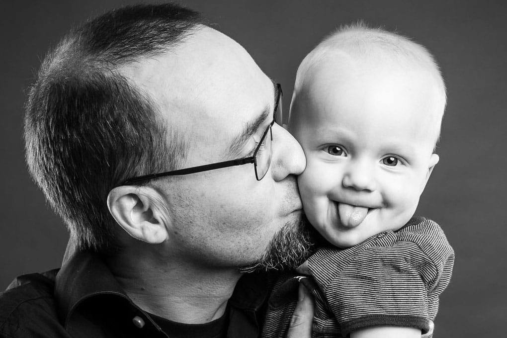Kinderfoto eines Jungen der die Zunge rausstreckt und von Papa geküsst wird, Familienfoto von Vater und Sohn